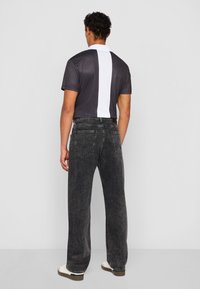 Chemise grise à manches courtes avec des rayures verticales blanches, assortie à un jean droit gris foncé. Les chaussures sont blanches avec des semelles brunes.