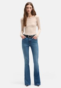 Beżowa bluzka z długim rękawem o prążkowanej fakturze, zestawiona z niebieskimi dzwonami w klasycznym stylu z pięcioma kieszeniami oraz czarnym paskiem z srebrną klamrą.