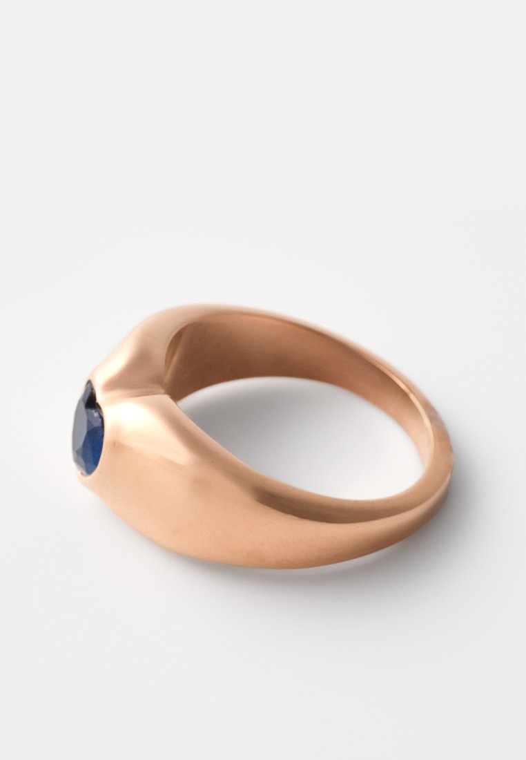 Anillo de oro rosa con un diseño liso y curvado, que presenta una gema ovalada azul montada en el centro. El acabado pulido realza su atractivo visual.