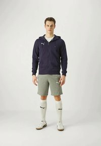 Morska zip-up hoodie, sivi šorts, bijele čarape i atletske cipele. Sadrži PUMA logo na odjeći i čarapama, glatke teksture.