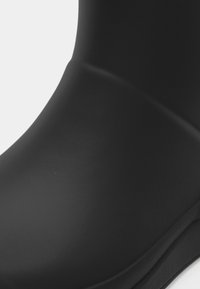 Fekete gumicsizma sima textúrával és kerek orral. Zökkenőmentes kialakítással és enyhén ívelt bokával rendelkezik a jobb illeszkedés érdekében.