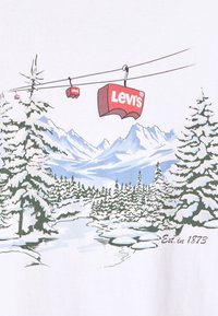 Bílá tričko s grafickým motivem zasněžených hor, stálezelených stromů a červených lanovek s nápisem "Levi's". Text "Est. v 1873" ve spodní části.