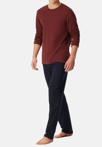 Burgundská košile s dlouhým rukávem zkombinovaná s námořnickými pyžamovými kalhotami s červeným geometrickým vzorem. Materiál vypadá měkce a má volný střih.
