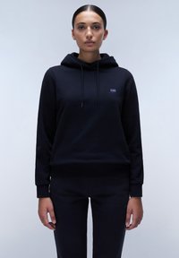 Zwarte hoodie van zachte stof met een trekkoordkap, geribbelde manchetten en een klein logo op de borst. Gecombineerd met bijpassende zwarte broek.