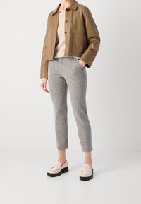 Bruine leren cropped jack, beige geribbelde trui, grijs gecheckte broek en lichtroze loafers met een zwarte zool. Soepele materialen en een op maat gemaakte pasvorm.