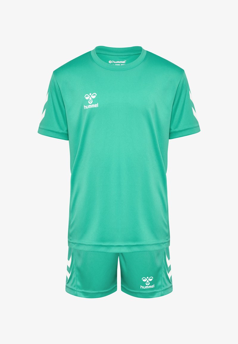 Tenue de sport verte en tissu léger. La chemise à manches courtes et le short présentent un logo blanc et des accents en chevron sur les manches et sur les côtés.