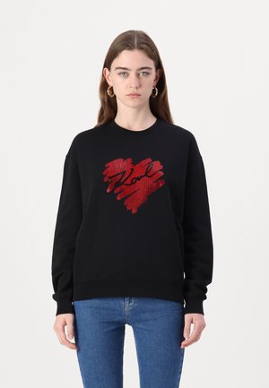 Zwarte sweatshirt met een rood hartontwerp in borstelafwerking en "Love" in zwarte schrift, gecombineerd met blauwe jeans.