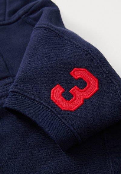 Temno modro blago z zloženim rokavom, na katerem je ob manšeti rdeča našitka s številko "3".