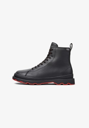 Stivale alto in pelle nera con suola rossa, dotato di lacci e una linguetta sul retro, esposto su uno sfondo bianco.