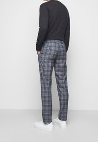 Grå rutiga byxor i lös passform, med knapp- och dragkedjestängning, sidofickor och en bakficka. Matchas med vita sneakers.