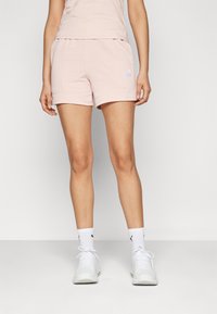 Light pink cotton shorts with an elastic waistband, side pockets, and a small blue logo on the left hem. Smooth texture and casual fit.