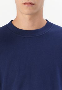 Granatowa koszulka typu crew neck wykonana z gładkiej tkaniny, o prostym wzorze i krótkich rękawach, z subtelnym detalem szwu na dekolcie.