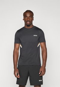T-shirt de sport noir avec un design texturé, à manches courtes, et un logo sur la poitrine. Associé à un short noir uni.