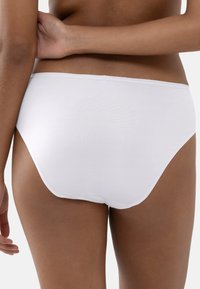 Woman wearing plain white high-waist underwear, showing lower back and hips, against a plain white background.