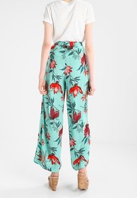 Kwiatowe spodnie o szerokich nogawkach, turkusowe tło z czerwoną i zieloną grafiką, elastyczny pas, lekki materiał, w połączeniu z sandałami na drewnianym obcasie.
