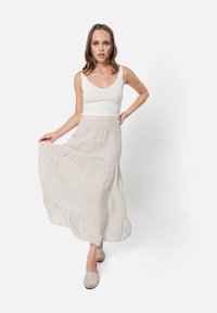 Gonna maxi in lino di un leggero beige con design a strati, vita elastica e texture fluida. Abbinata a scarpe slip-on beige.