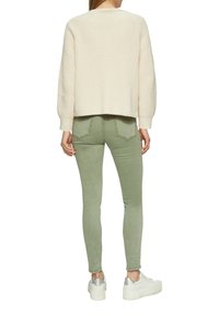Crème gebreide trui met een cropped ontwerp, gecombineerd met groene aansluitende broek. Schoeisel heeft een chunky witte zool met zilveren accenten.