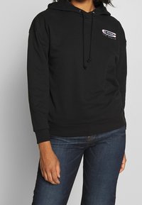 Černá mikina s kapucí, s logem na přední straně, s tkaničkovou kapucí a žebrovanými manžetami. Volný střih, vyrobena z měkké, texturované tkaniny.