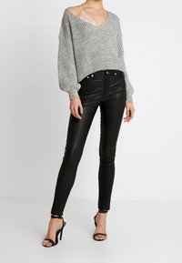 Grå överdimensionerad stickad tröja med V-ringning, i kombination med formpassande svarta läderbyxor och svarta klacksandaler.