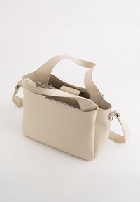 Beige, strukturiertem Lederbeutel mit breiter Öffnung, verstellbarem Tragegurt und Reißverschlussverschluss. Hat ein minimalistisches Design ohne sichtbare Metallteile.