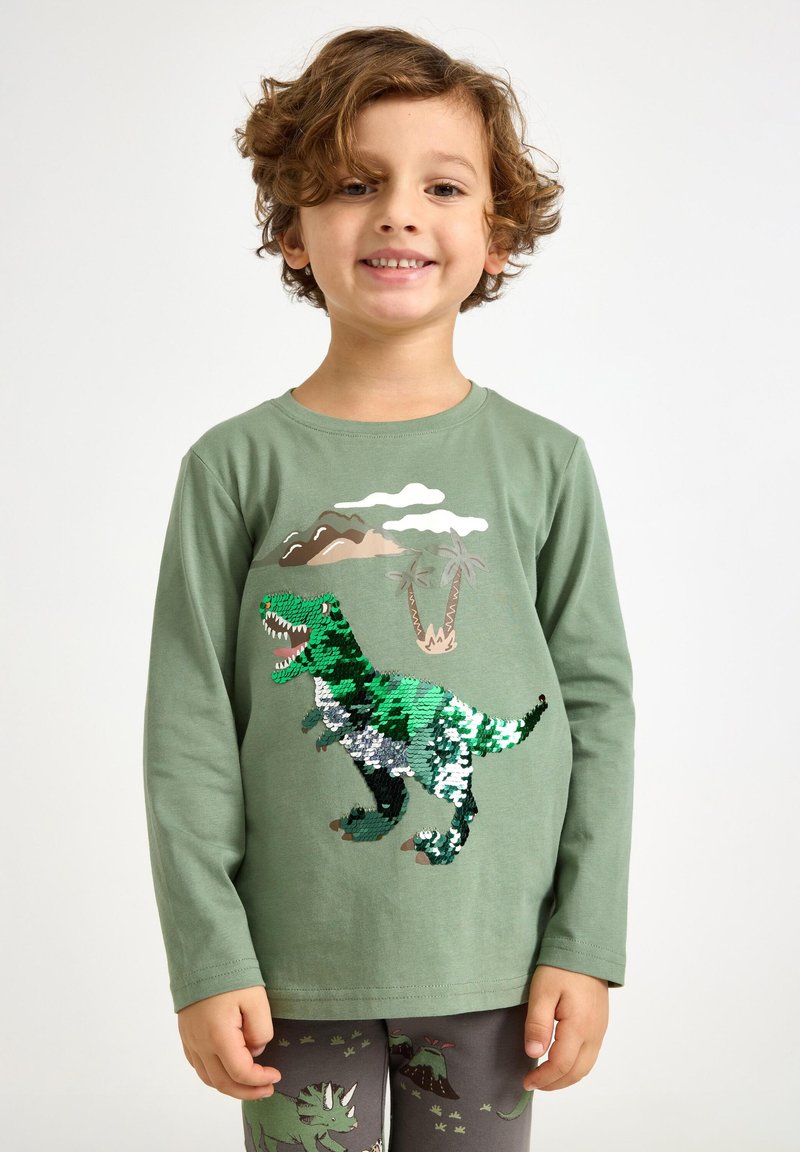 Grøn langærmet t-shirt med en paljetteret dinosaurgrafik. Blødt bomuldsmateriale med motiver af bjerge og palmetre6er i baggrunden.