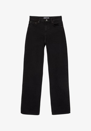 Femme portant un crop top blanc à manches courtes noué, un jean noir ample taille haute et des chaussures noires, debout les mains sur les hanches.