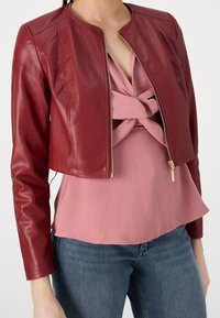 Rote, lederne, cropped Jacke mit rundem Ausschnitt und goldfarbenem Reißverschluss. Trägt man über einem roten Oberteil mit verdrehtem Design und ausgestelltem Saum.