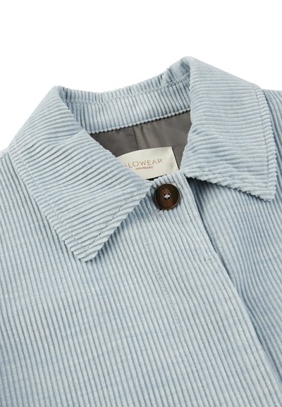 Jasnoniebieska kurtka z kordurowego materiału z kołnierzykiem, charakteryzująca się prążkowaną teksturą i brązowym zapięciem na guziki. Etykieta widoczna wewnątrz.