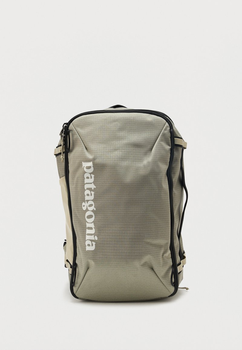 Rechteckige beige Patagonia-Duffelbag mit schwarzen Reißverschlussumrandungen und weißem vertikalem Logo auf der Vorderseite, vor einem schlichten weißen Hintergrund.