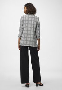 Blazer cinzento às riscas com design estruturado, mangas arregaçadas e corte reto, combinado com calças largas pretas e sandálias pretas de salto bloco.