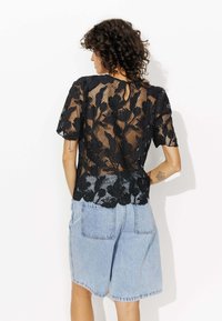 Top en dentelle florale noire à manches courtes avec un détail en forme de clé au dos, associé à un short en denim bleu clair.