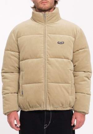 Beige corduroy puffer jacket with high collar, zip closure, and stitched panels. Features a black logo patch on the chest.