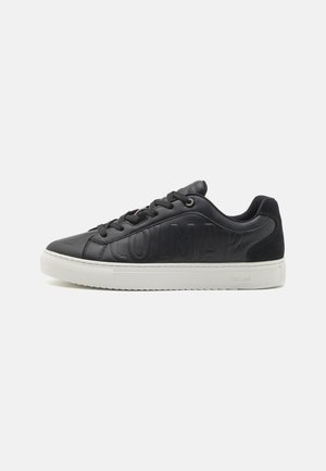 Zapatillas negras de cuero con una textura lisa, que presentan el logotipo "COLMAR" en relieve, suela de goma blanca y cordones negros.