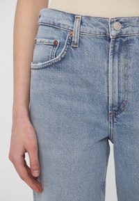 Vaqueros de mezclilla azul claro con cintura alta, diseño de cinco bolsillos, herrajes de tono cobre y una sutil textura descolorida.