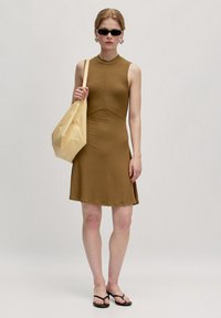 Braunes geripptes ärmelloses Kleid mit einem hohen Kragen, ausgestelltem Rock, kombiniert mit einer beigen lässigen Tasche und schwarzen Flip-Flops. Schwarze Sonnenbrille getragen.