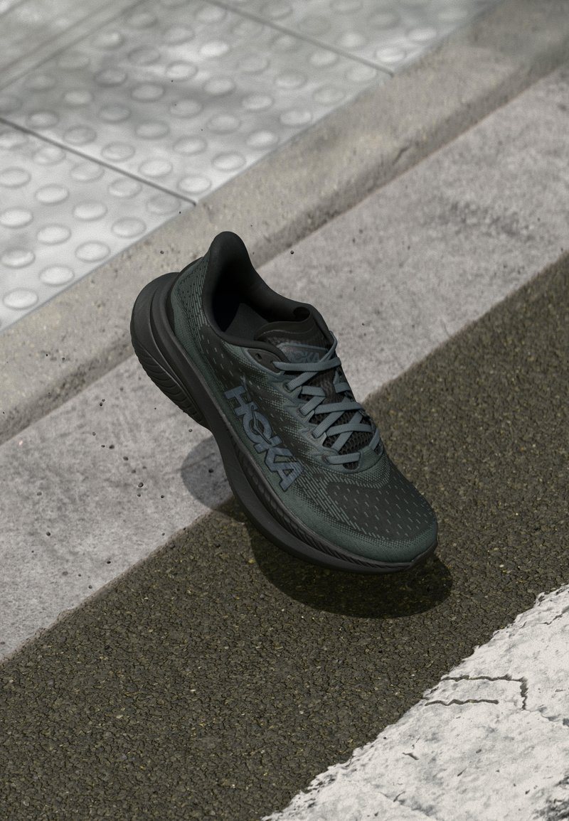 Black running shoe with mesh upper, textured accents, and logo, featuring a cushioned sole and gray laces, positioned on pavement.