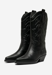 Botas de cowboy de cuero negro con punteras puntiagudas, costuras decorativas y un ligero tacón. Superficie texturada con tirantes en la parte superior.
