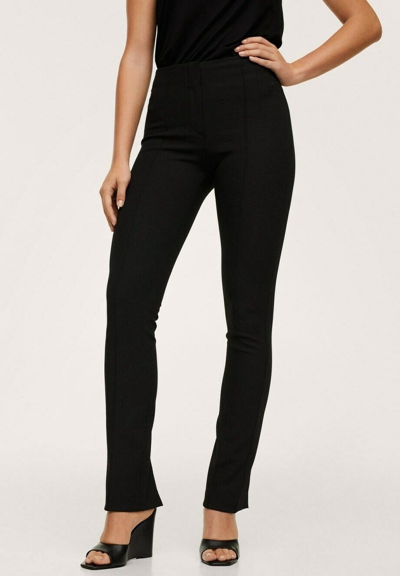 Černé kalhoty s vysokým pasem a úzkým střihem, s hladkou texturou a šitím na míru. V kombinaci s černými sandály na platformě.