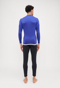 UV-beskyttende langermet rash guard i blått med kremfarget kant, sammen med svarte tettsittende leggings. Glatt, elastisk stoff for komfort.