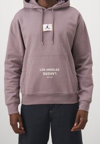 Felpa viola con cappuccio, tasca frontale e polsini a coste. Presenta un patch con logo e il testo "LOS ANGELES LAKERS EST. 1960" in bianco.