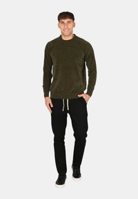 Maglia verde a maniche lunghe con texture e scollo rotondo, abbinata a pantaloni jogger neri con elastico in vita e coulisse, e sneakers nere.