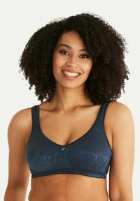 Marinblå trådlös BH tillverkad av texturerat tyg, med ett subtilt mönster, breda axelband och en liten dekorativ accent i mitten.