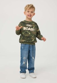 Zielony sweatshirt w kamuflażu z nadrukiem "DINO ROAR!", w połączeniu z jasnoniebieskimi przetartymi dżinsami i białymi trampkami. Zaprojektowany dla dzieci.
