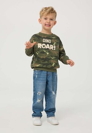 Felpa verde camouflage con stampa "DINO ROAR!", abbinata a jeans chiari strappati e sneaker bianche. Progettata per i bambini.
