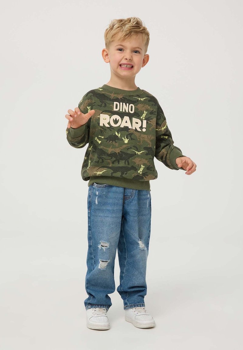 Zielony sweatshirt w kamuflażu z nadrukiem "DINO ROAR!", w połączeniu z jasnoniebieskimi przetartymi dżinsami i białymi trampkami. Zaprojektowany dla dzieci.