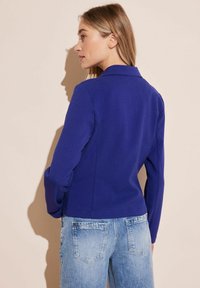 Dopasowana niebieska marynarka z kołnierzykiem, usztywnionymi ramionami i długimi rękawami, w połączeniu z jasnoniebieskimi dżinsami.