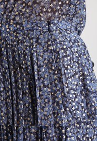 Vestido de flores azules con detalles dorados, diseño plisado y un cierre lateral oculto. Presenta una tela suave y texturada.