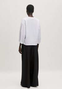 Witte, loszittende top met lange, opgezette mouwen; gecombineerd met brede zwarte broek. Glad textuur, minimalistisch ontwerp.