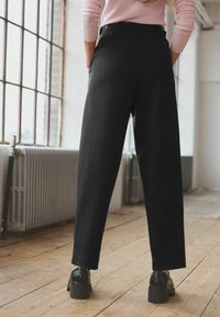 Zwarte broek van een gladde stof, met een hoge taille, twee achterzakken en een rechte pijp, gecombineerd met zwarte hakken.