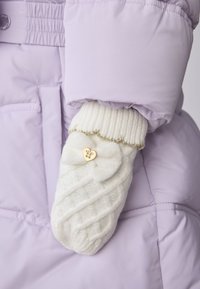 Fehér kötött kesztyűk texturált mintával, arany szív alakú gombdíszítéssel és aranyszálas hullámos szegéllyel, lila dzsekivel viselve.